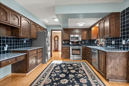 Spacious eat-in kitchen featuring rich wood cabinetry, stainless steel appliances, generous storage, granite counter-tops & hardwood floors. The open layout flows beautifully into the surrounding living spaces.