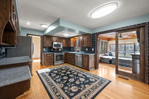 Spacious eat-in kitchen featuring rich wood cabinetry, stainless steel appliances, generous storage, granite counter-tops & hardwood floors. The open layout flows beautifully into the 4-season sun room!!!