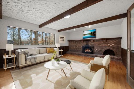 CGI pic of Character-filled main-level family room featuring hardwood floors, rich wood beams, textured walls, a large picture window that fills the space with natural light, and a striking full brick fireplace