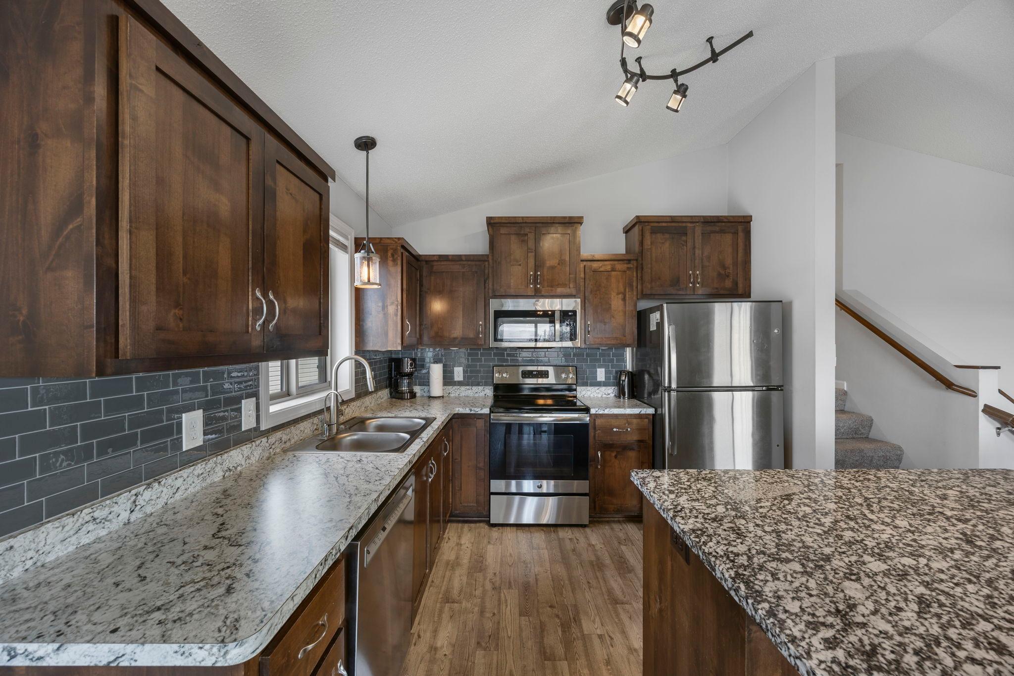 The kitchen features stainless steel appliances, a tile backsplash, and dark wood cabinetry, creating a warm and inviting feel