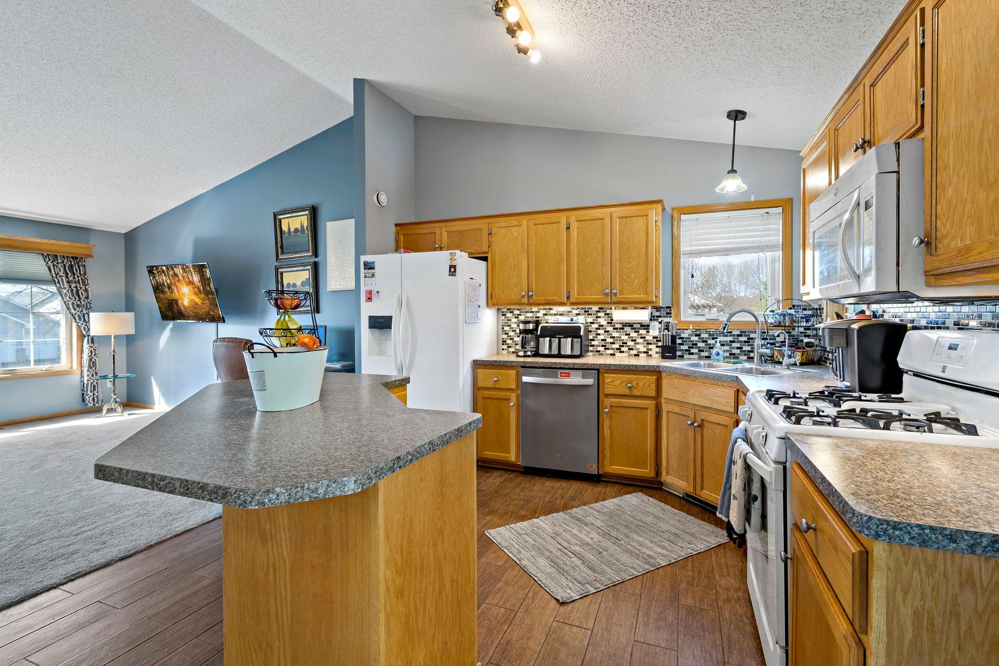 Large open kitchen area with corner window and sink, vaulted ceilings, and some newer appliances.