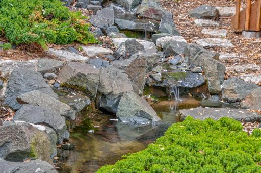 The tranquil water feature flows under the arched bridge to the koi pond.