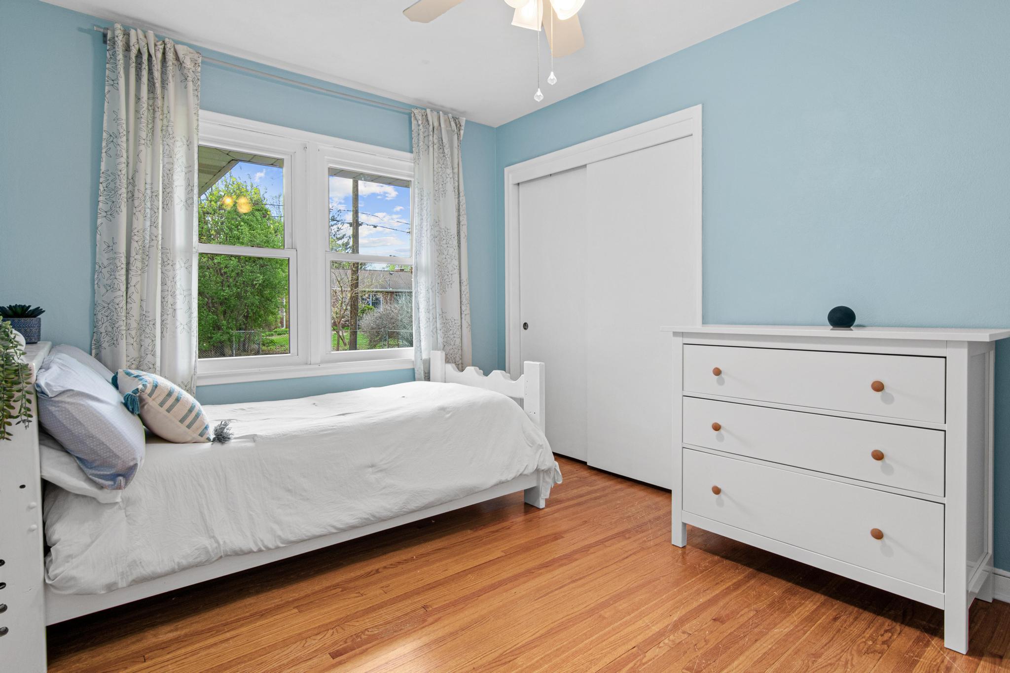 Bedroom 2 of 3 on the main floor features hardwood floors, white millwork and a ceiling fan. There is plenty of room for a bed, desk, and dresser in here and it has a spacious closet too!