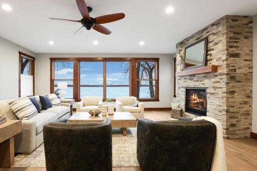 The spacious living room exudes both comfort and sophistication, anchored by a gas fireplace with an eye-catching stone surround and framed by uninterrupted lake views.