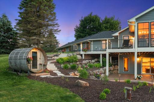 Twilight exterior, barrel sauna lit up, stone path, warm glow. Truly dreamy.