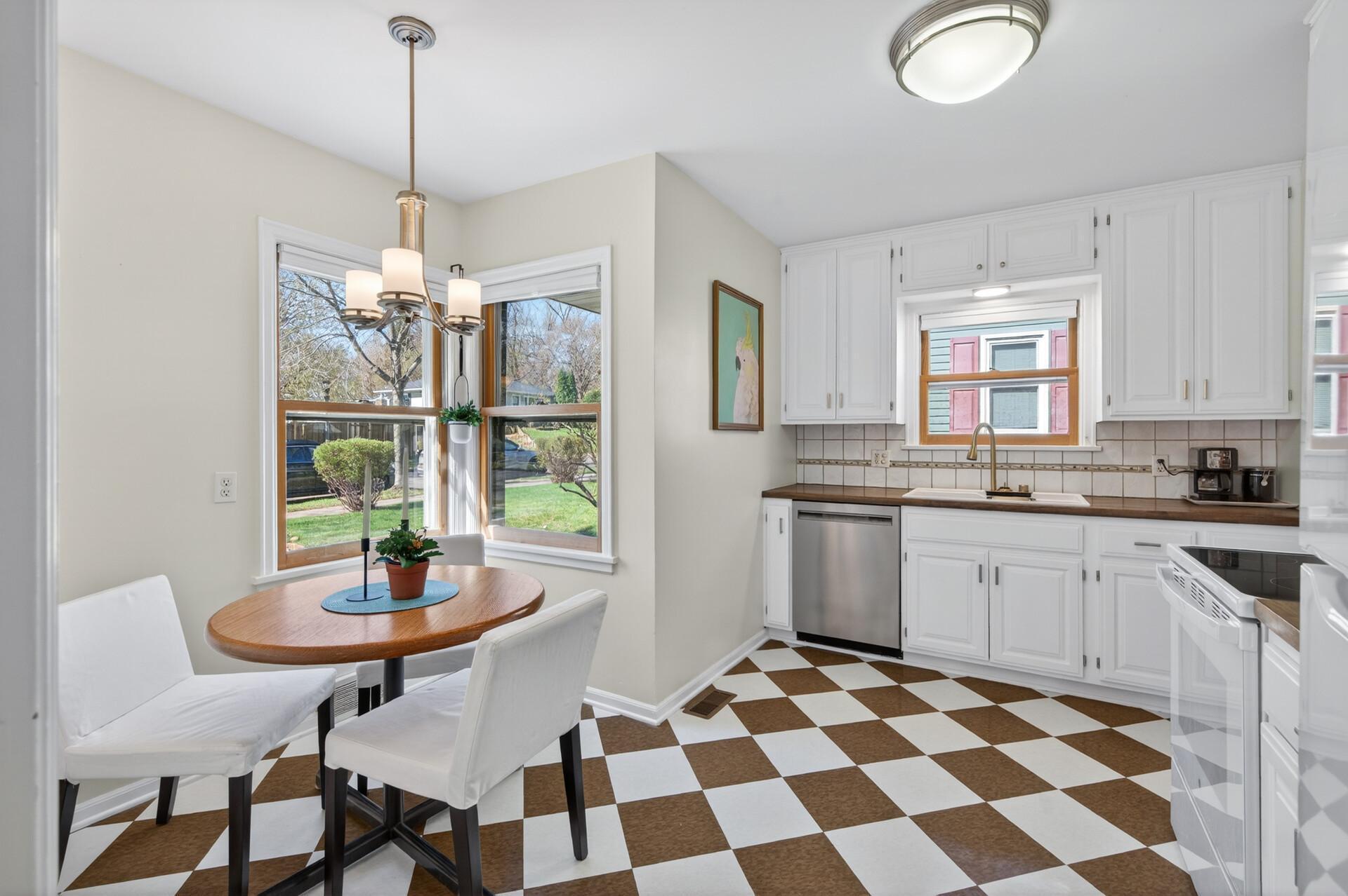 Look at this light and bright kitchen with brown checkerboard floor and eating area with corner windows.
