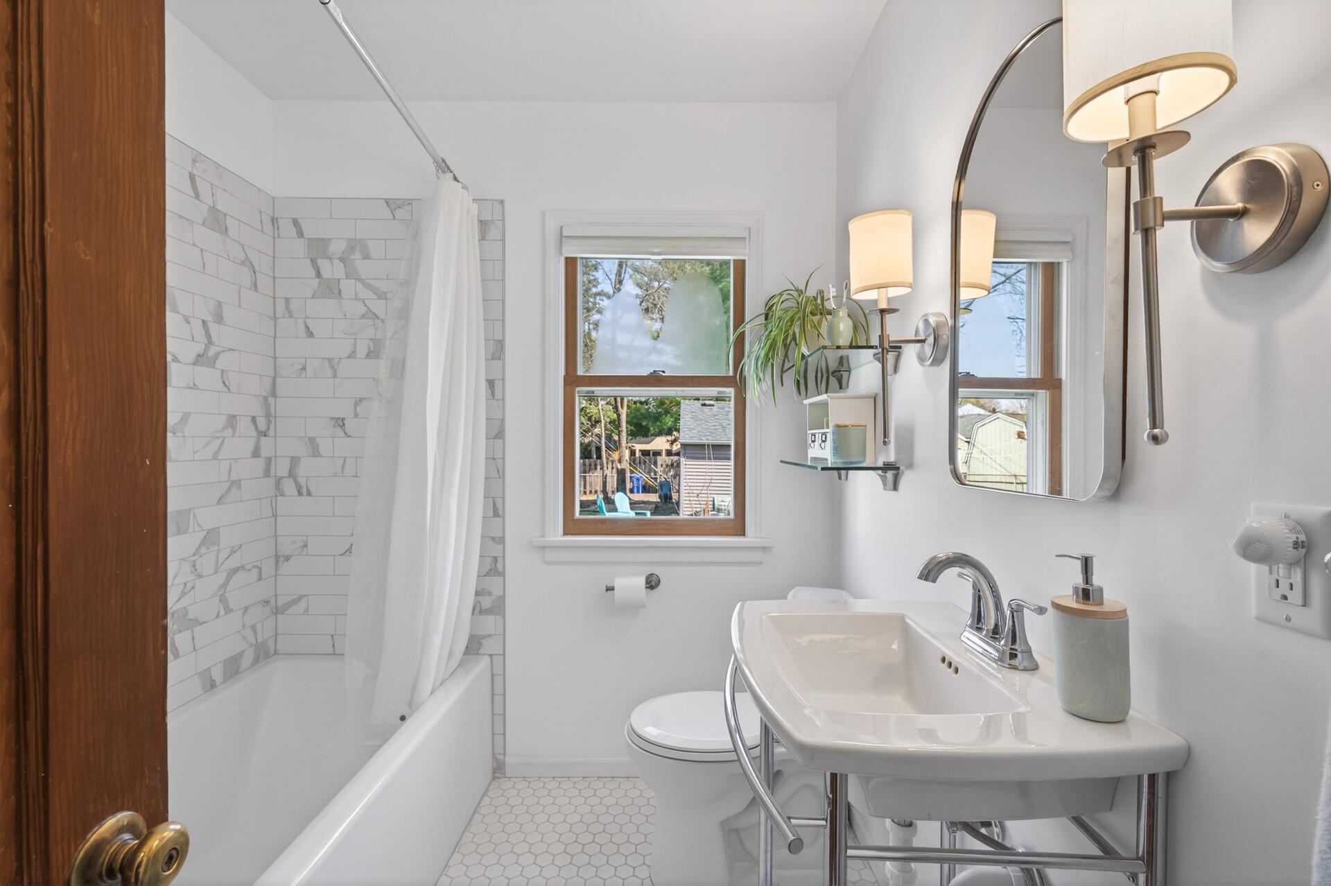 Tastefully renovated bathroom with marble tile in the tub and shower and ceramic hex tile on the floor. Everything is fresh and light and new!
