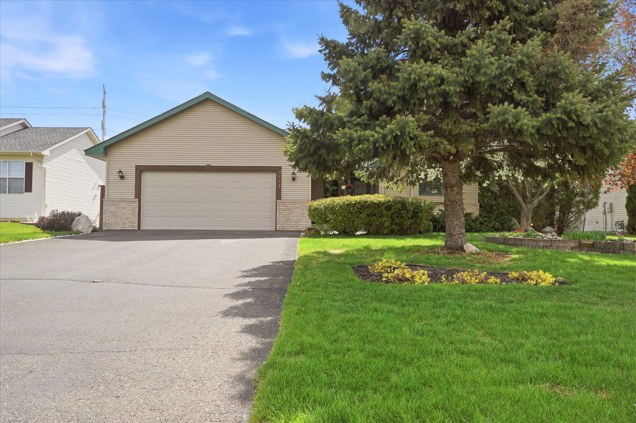 A wide front lawn, mature tree, and spacious driveway create a balanced and inviting exterior.