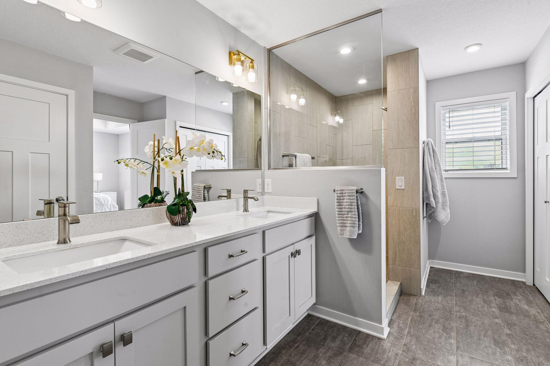 Primary bathroom has dual vanities, tiled walk in shower and large walk in closet