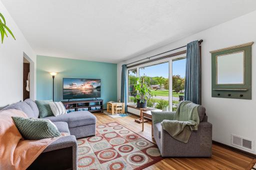 A spacious living room opens up around a massive picture window that floods the space with soft, golden natural light.