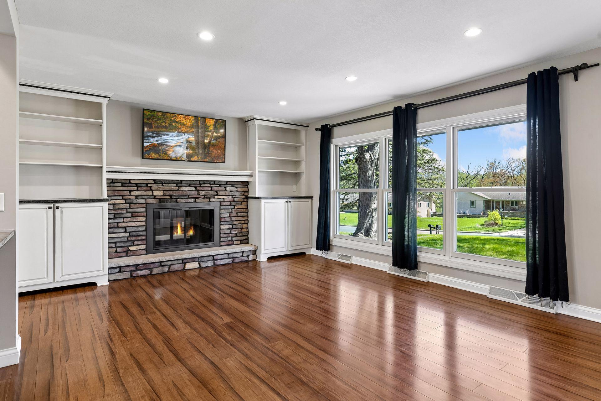 Bright and airy living room with near floor to ceiling windows, wood burning fireplace and gleaming luxury hardwood floors.