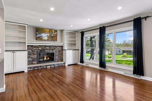 Bright and airy living room with near floor to ceiling windows, wood burning fireplace and gleaming luxury hardwood floors.