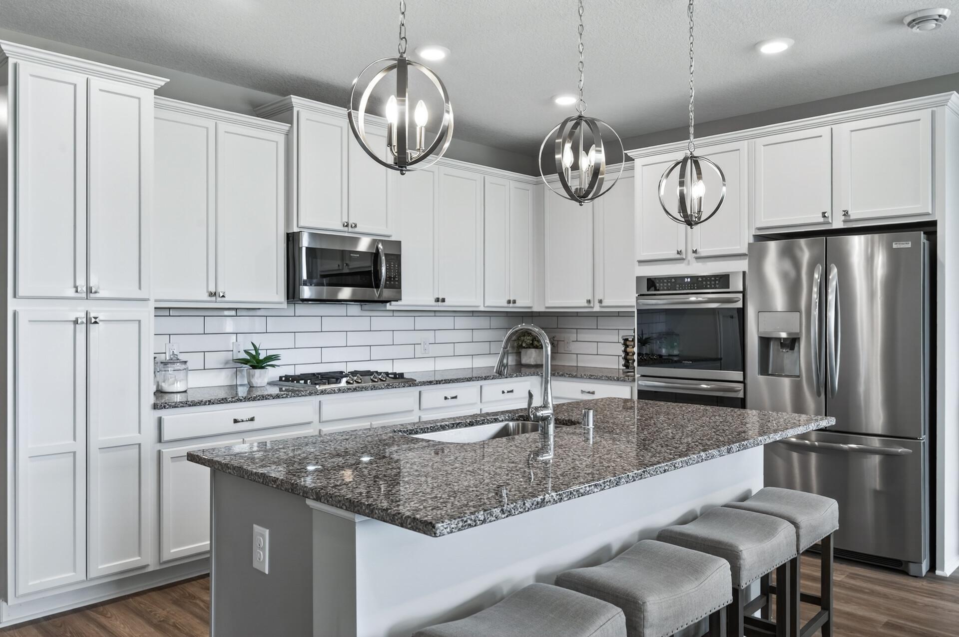 Crisp white cabinetry kitchen with large granite countertops with bar stools, white backsplash and upgraded refrigerator with filtered water.