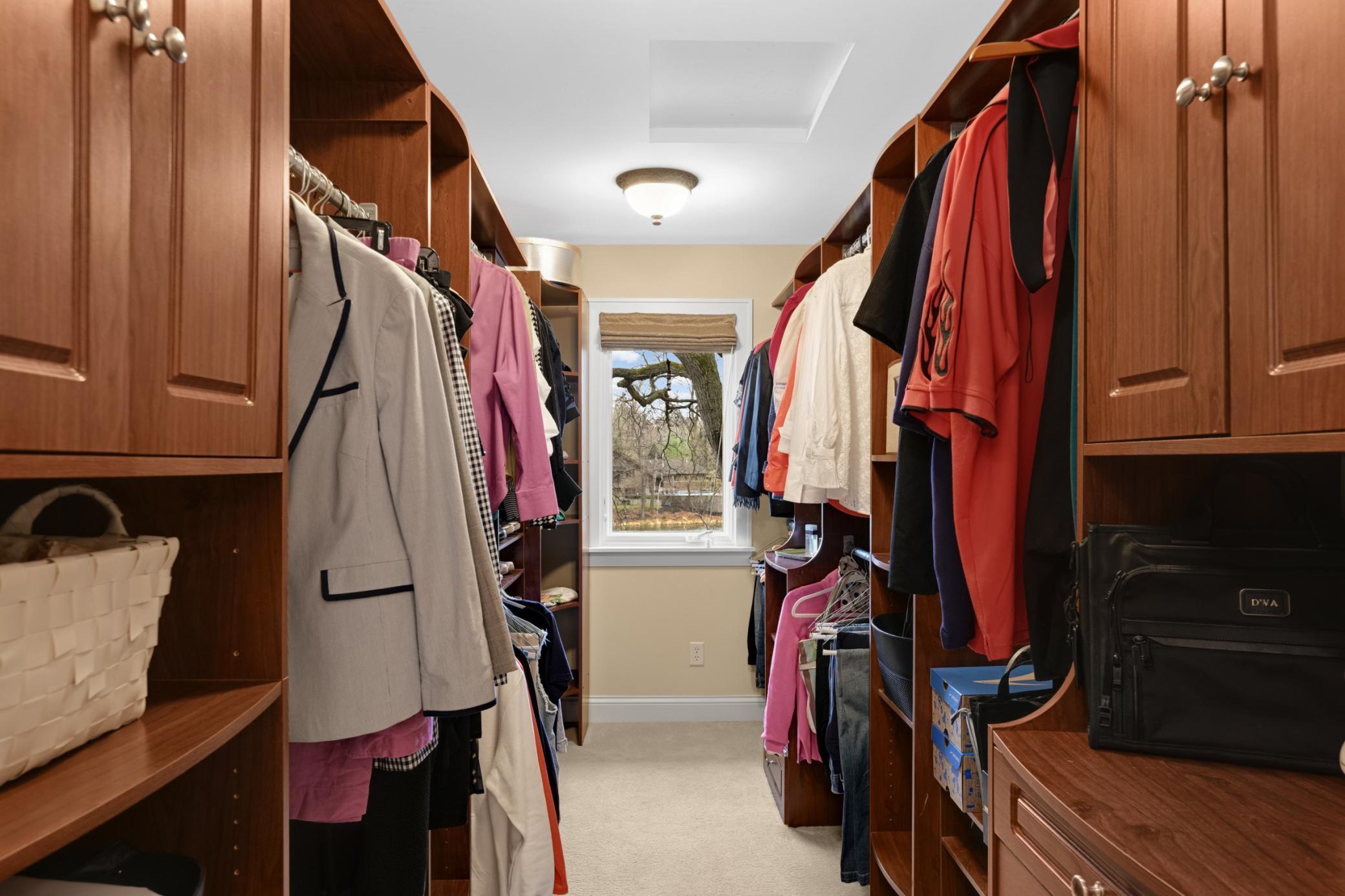 A large walk-in primary closet with custom organizers and a window for natural light.