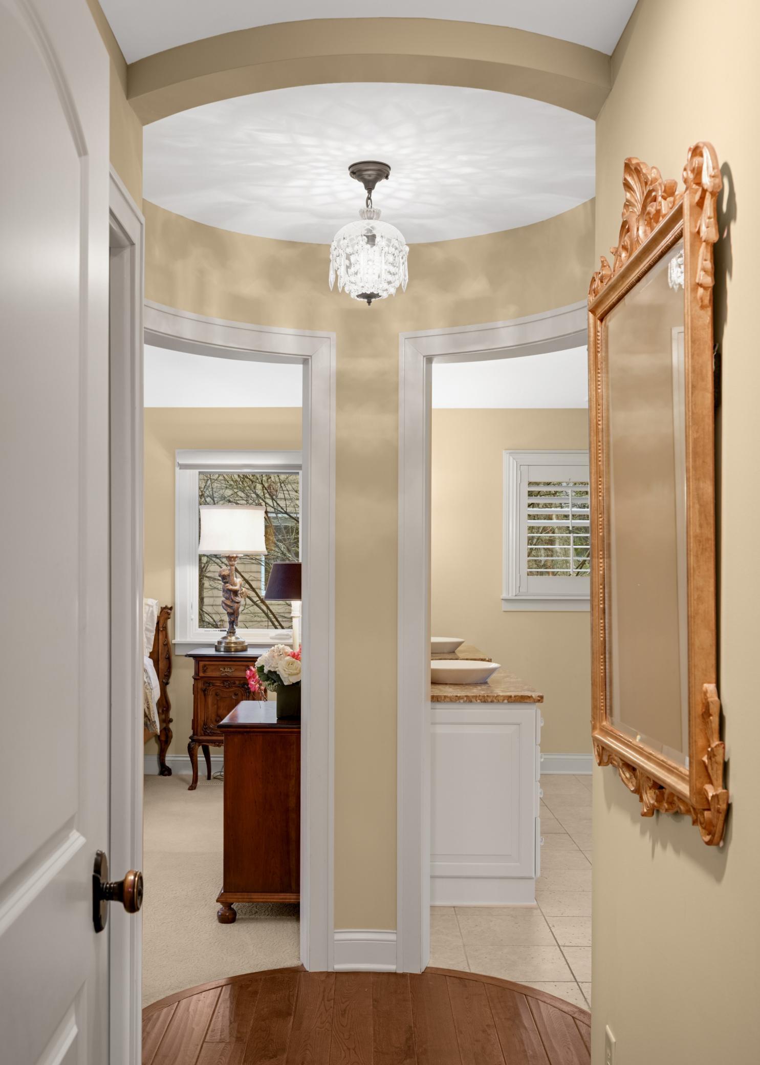 A hallway to the vaulted primary suite ends in a curved wall flanked by two doorways