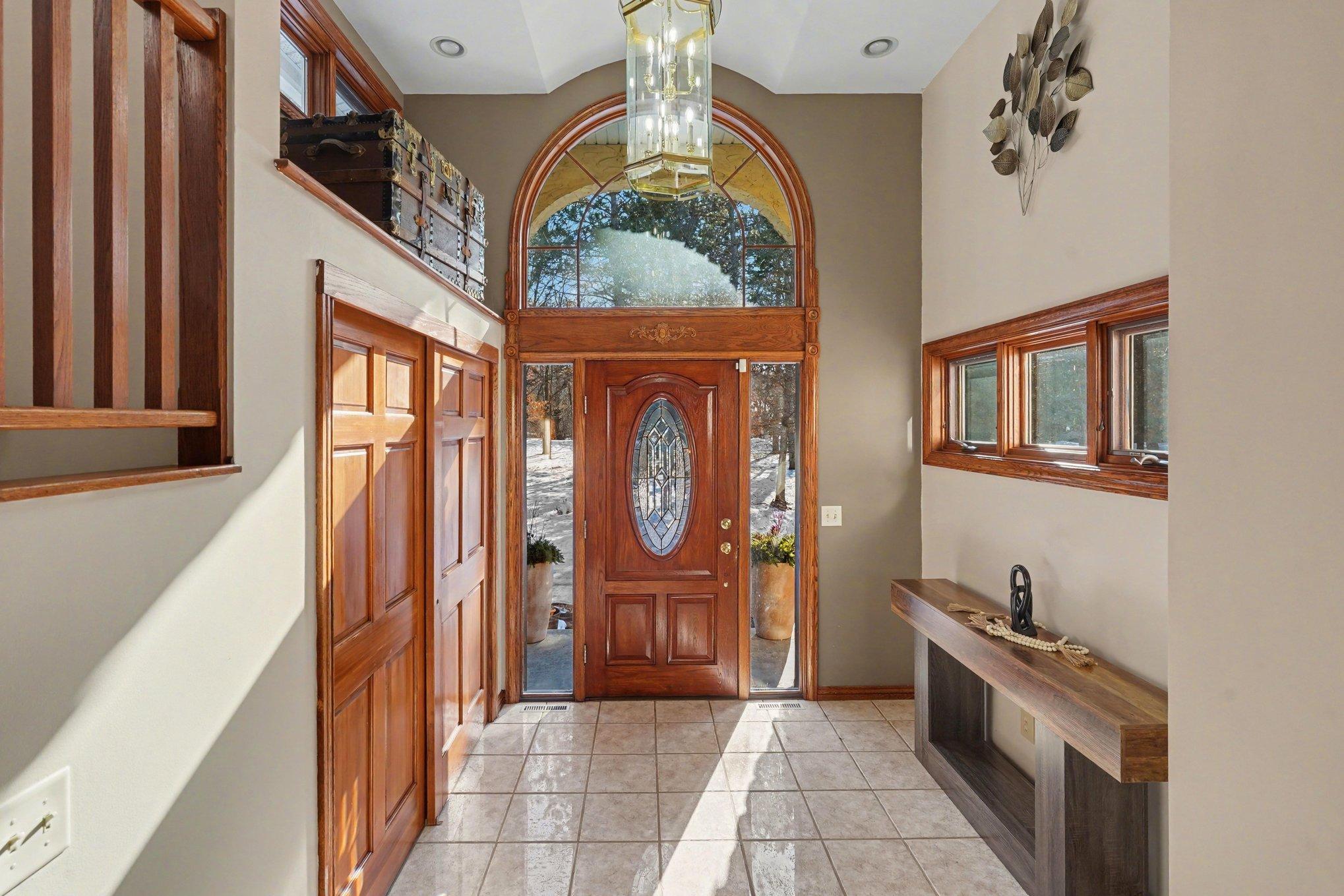 A grand foyer welcomes you w/soaring 12'5" vaulted barrel ceilings & lots of natural light streaming through a large arched window, transoms, and sidelights. This bright, inviting entry features durable ceramic tile floors & a convenient coat closet.