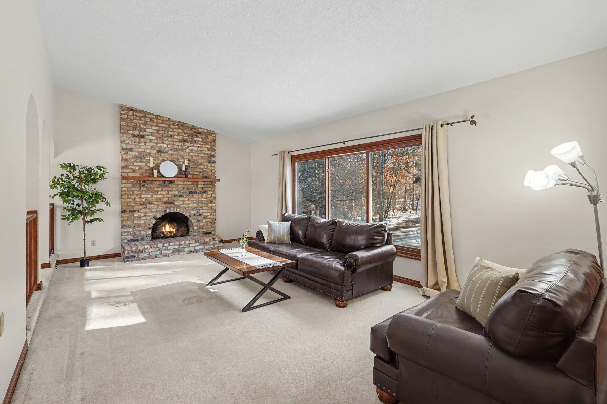 Bright living room features vaulted ceilings, a brick wood-burning fireplace, and a large window overlooking the wooded front yard. Flooded with natural light, this space flows seamlessly into the formal dining room.