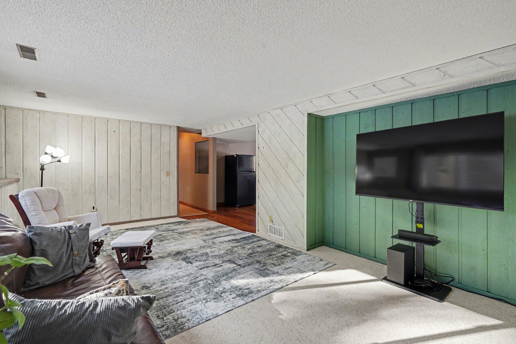 This view shows the lower-level family room's seamless flow into the additional entertaining space. A perfect layout for hosting large gatherings and game days! The under-stairs storage includes add'l sunken storage space.