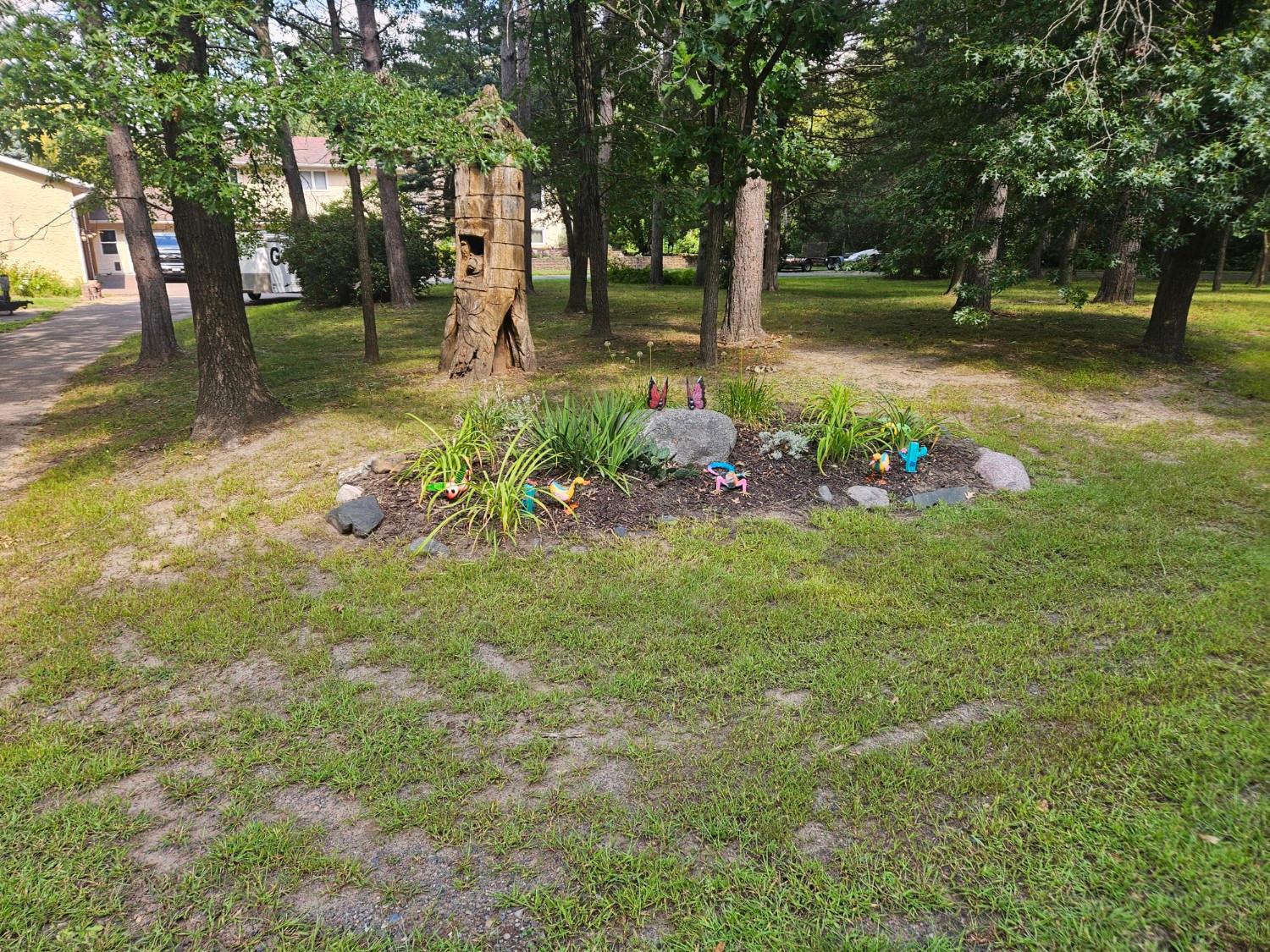 The home features a horseshoe driveway with mature trees adding privacy. It's decorated with a tree carving and garden.