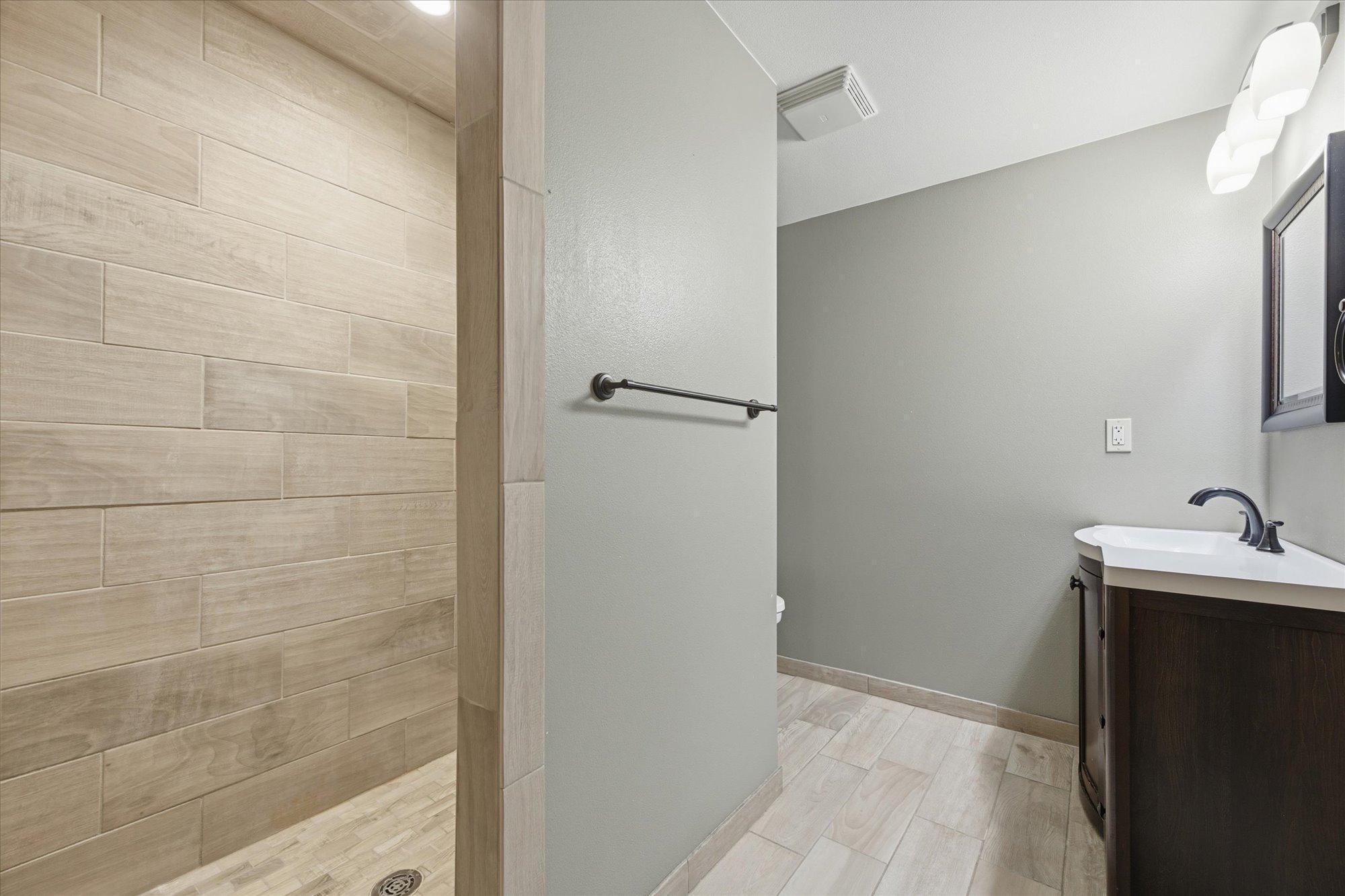 Lower-level bathroom with tile flooring, a spacious walk-in tiled shower, and a sleek vanity for a clean, modern feel.