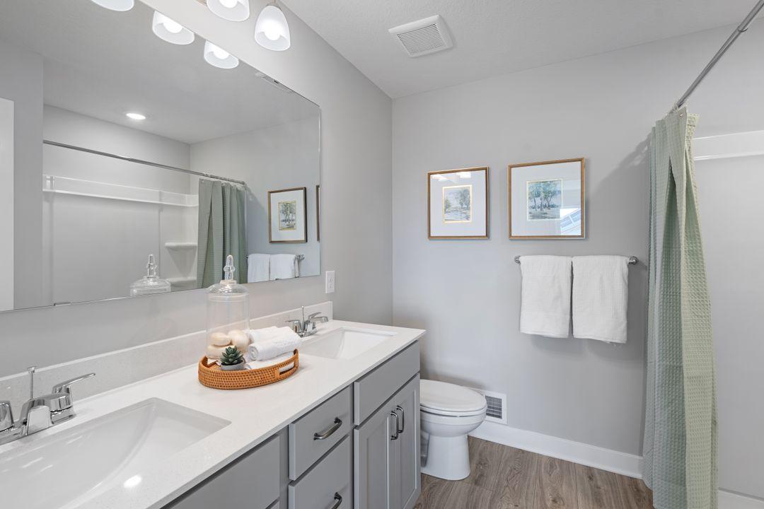 A peak inside the bathroom off the Primary Suite. Notice the extra high cabinets and double-bowl Quartz covered vanity with loads of storage! Photo is of model home. Colors and options may vary. Ask Sales Agent for details.