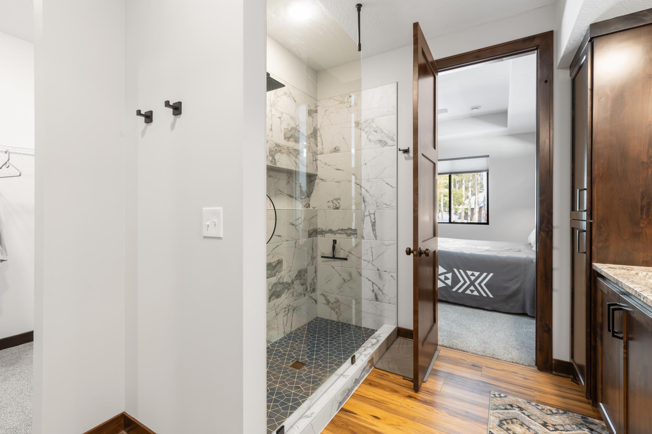 Rich stone and wood finishes ground the primary suite in both the home’s design and its natural surroundings. To the left, you also see the oversized walk-through primary closet.