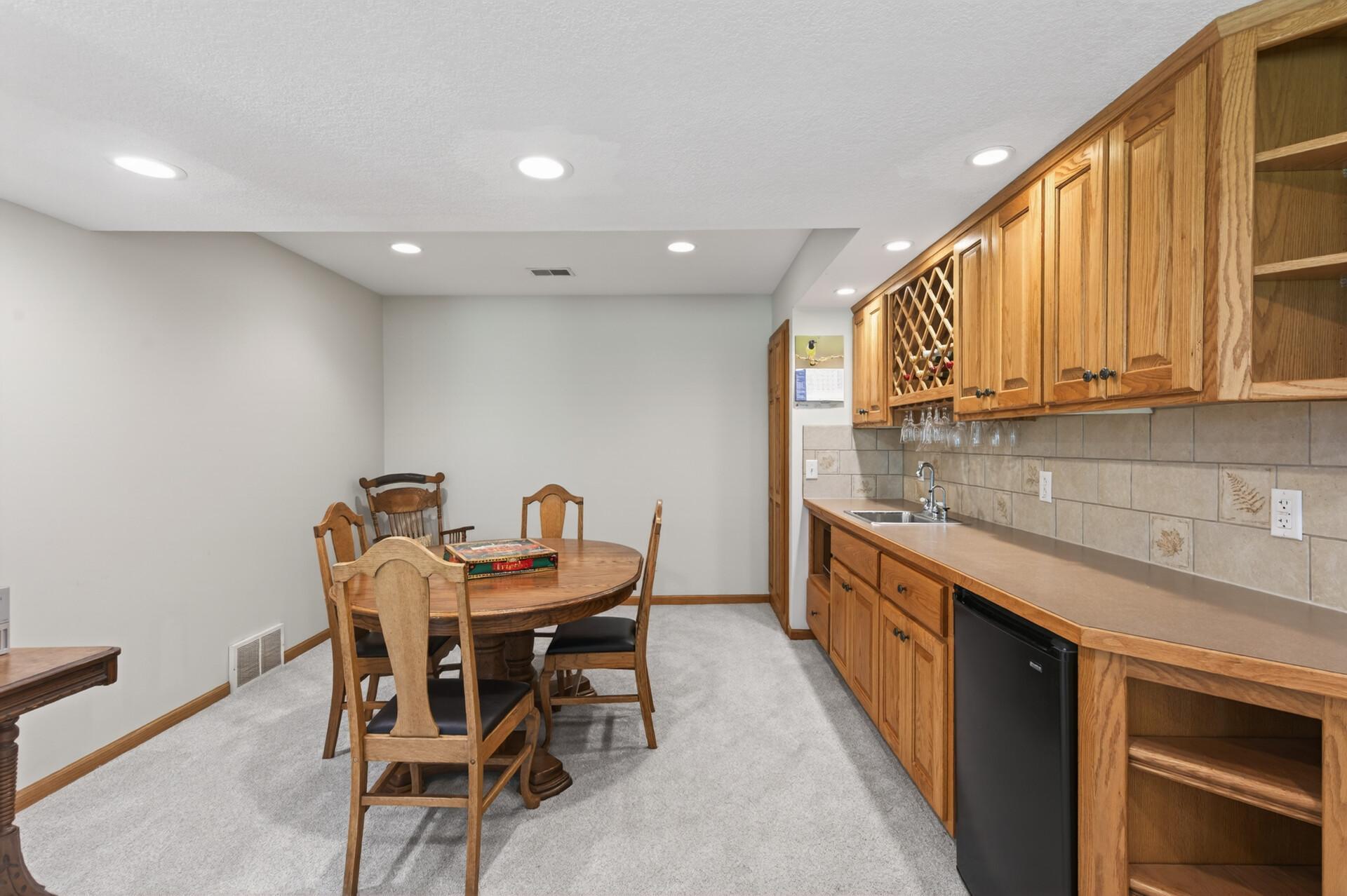 Lower level game area with a built-in wet bar, wine & glass rack, mini fridge & tile backsplash.