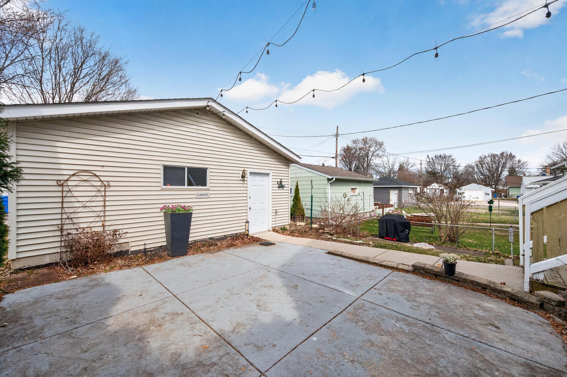 Detached garage with convenient access from the patio, complemented by low-maintenance landscaping and outdoor lighting.