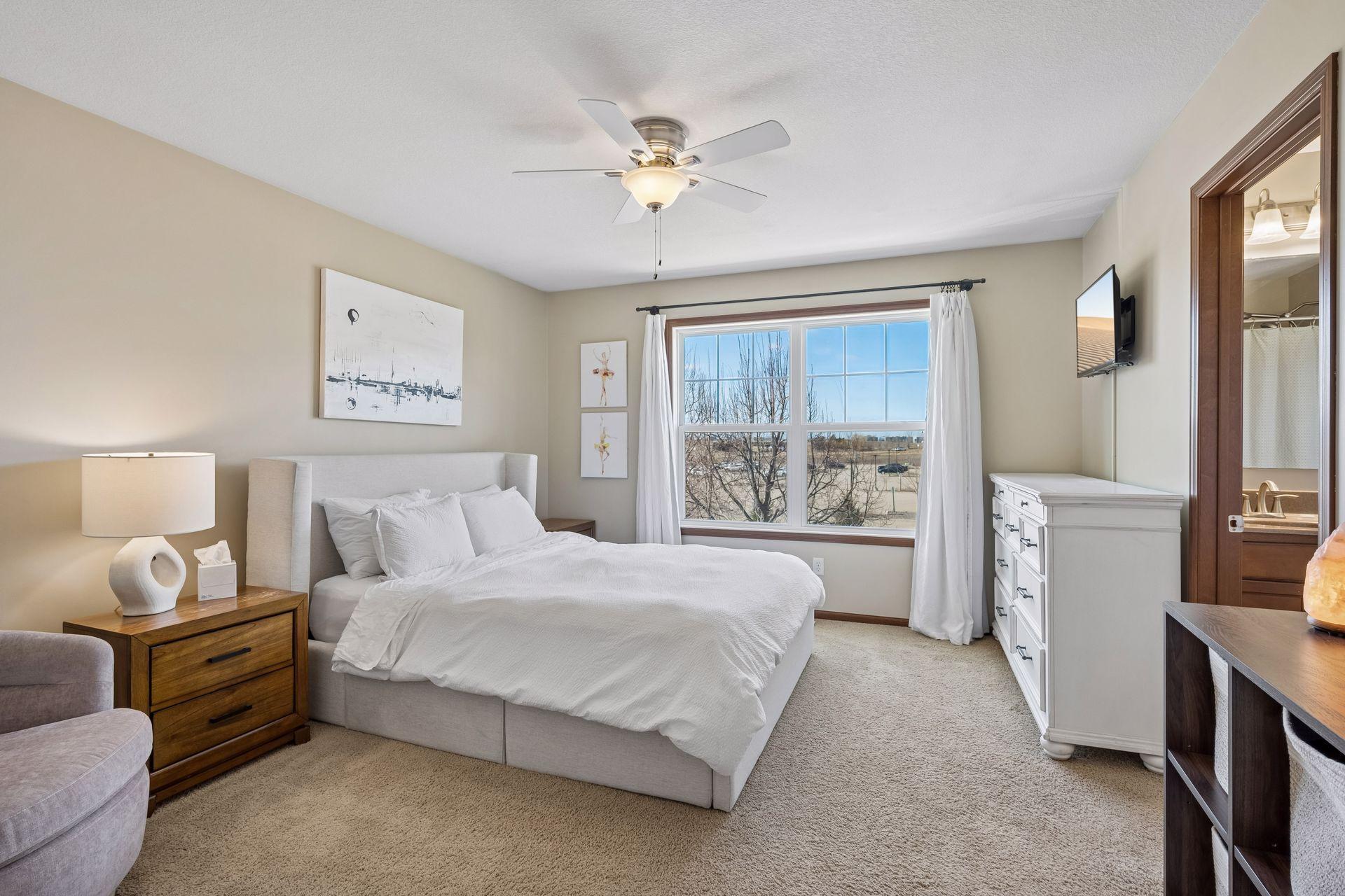 Roomy primary bedroom with large windows, space for dressers and reading chair.