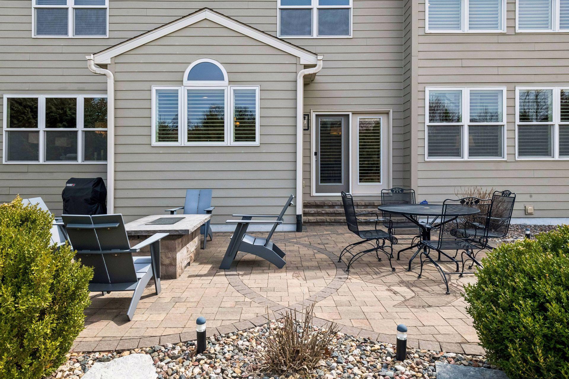 Landscaped backyard with paving stone patio, fire pit, and peaceful green space views.
