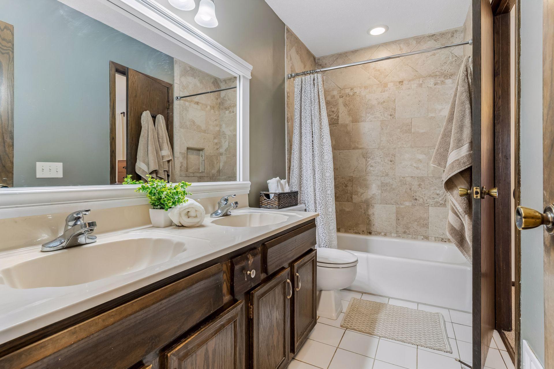 Upper-level full bathroom with double vanity, tile flooring, and tiled shower/tub surround.