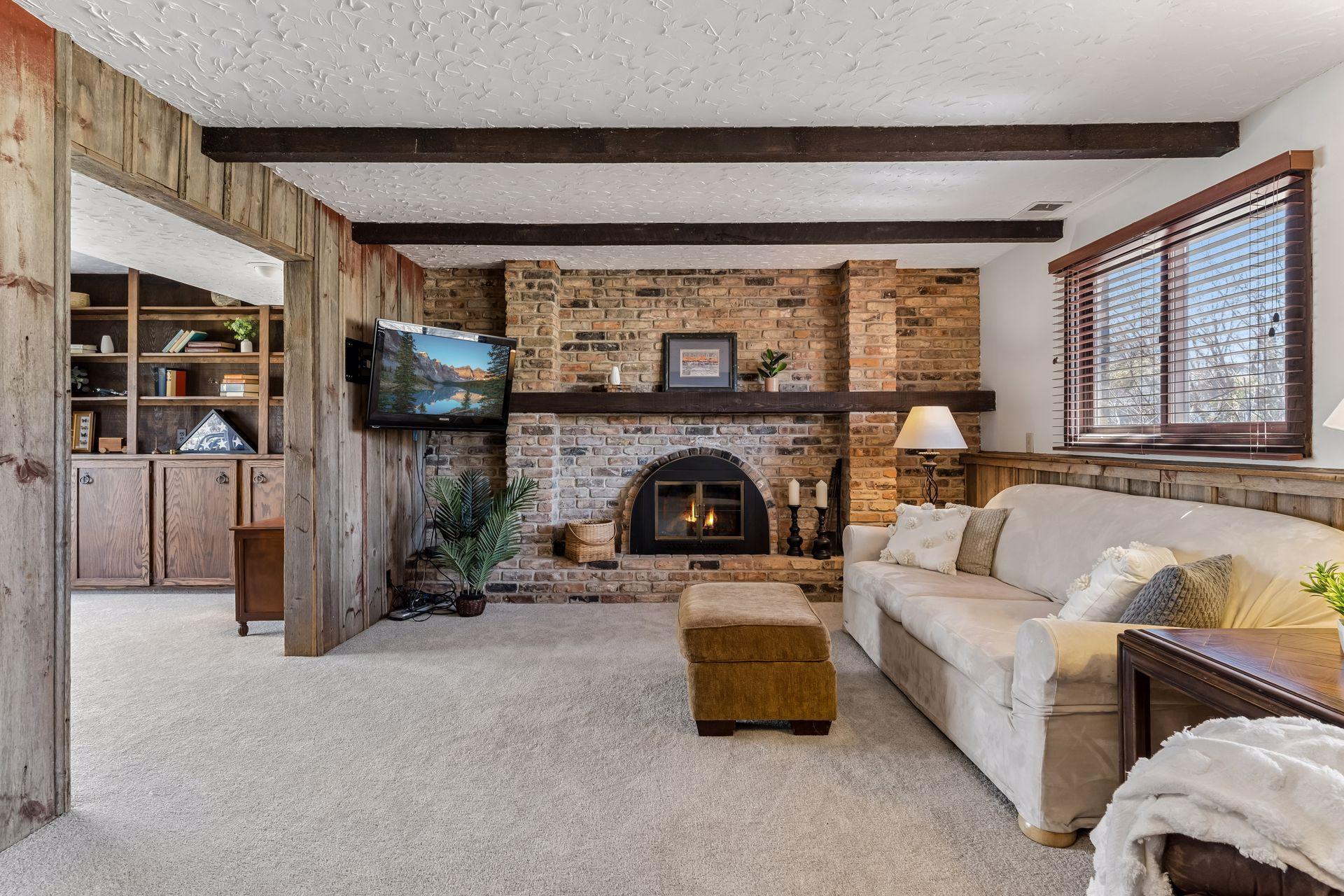 Lower-level family room featuring brick wood-burning fireplace, exposed wood beams, and new carpeting, creating a warm and inviting living space.