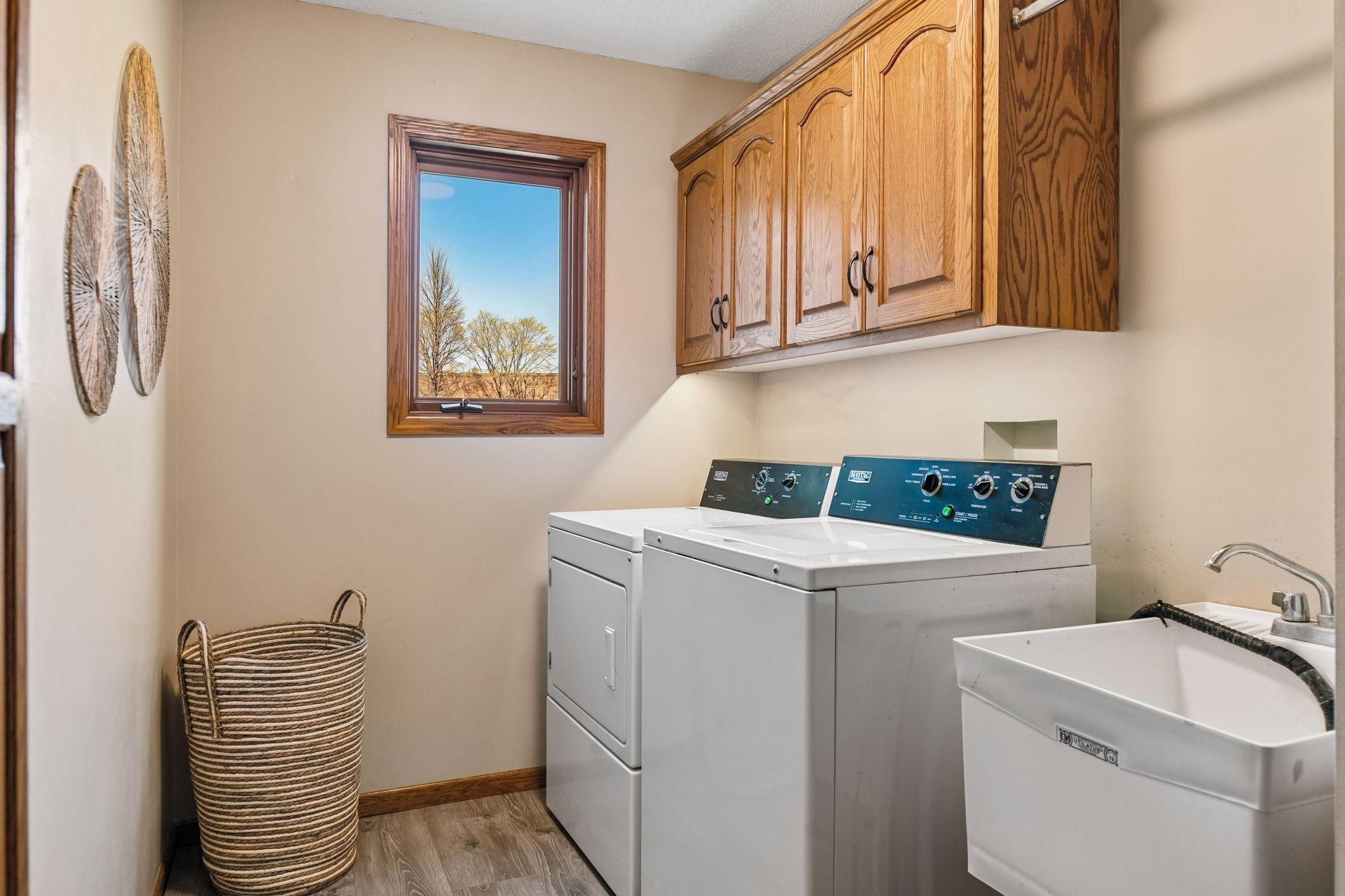 Laundry room located on the main level boasting LVP flooring, utility sink, and storage cabinets.