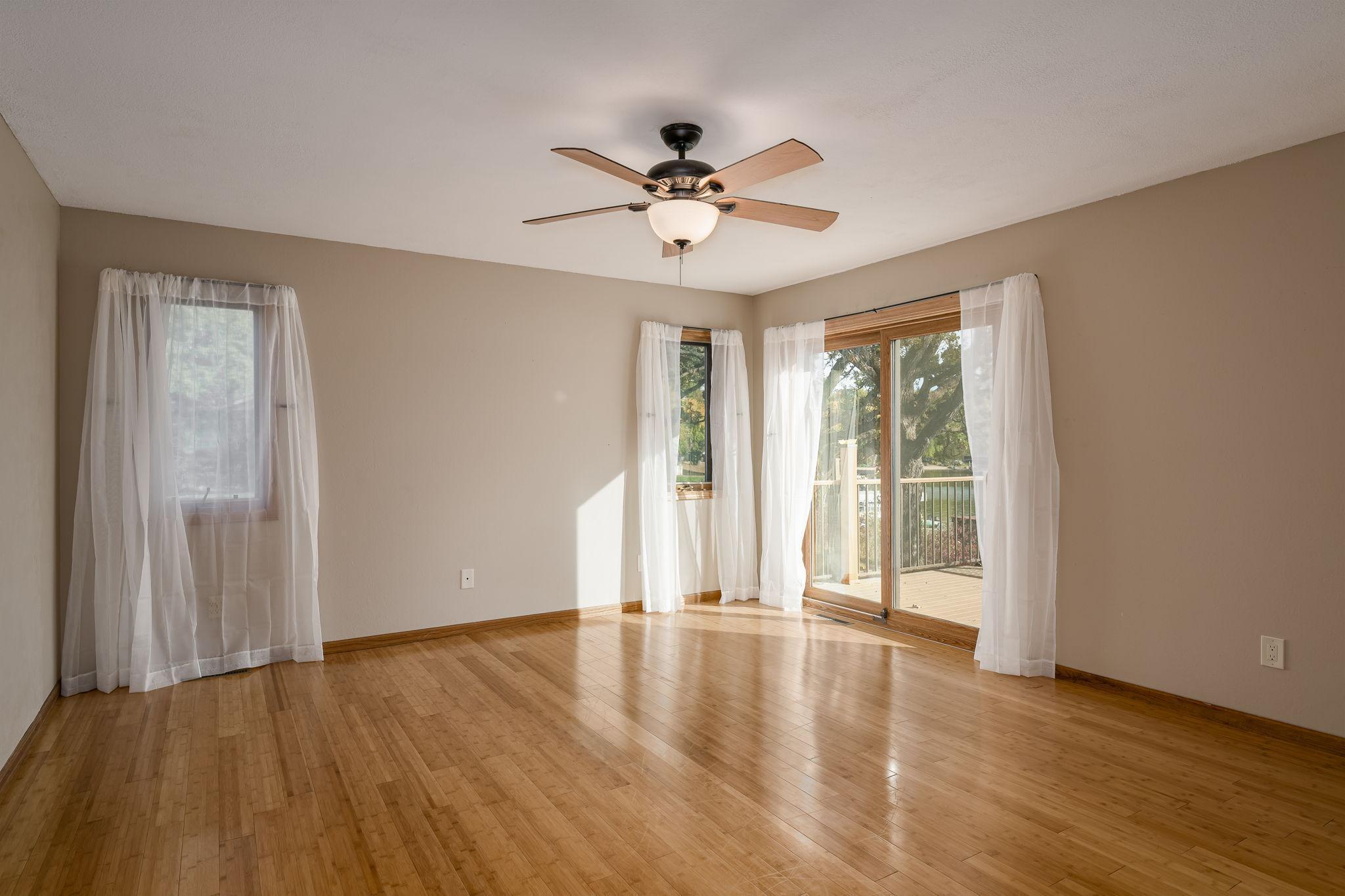 The main floor primary suite features luxurious bamboo wood floors and a sliding glass door that opens onto a massive deck, offering direct access and stunning lake views.