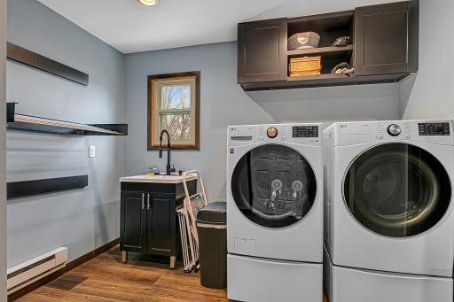 With a front-load LG ThinQ washer and dryer with storage drawers, a utility sink, wall-mounted drying racks, and updated flooring this area is as practical as it is polished.