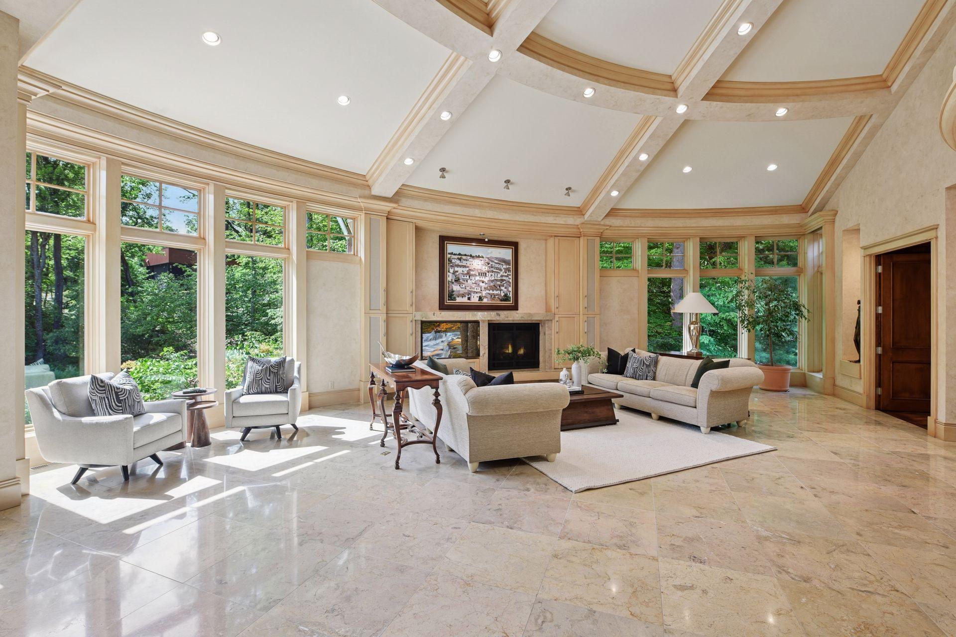 Oversized great room featuring a vaulted, beamed ceiling, walls of windows, and an expansive fireplace. Grand yet cozy, with multiple inviting seating areas.
