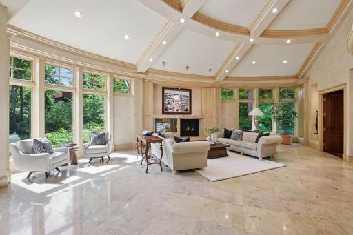 Oversized great room featuring a vaulted, beamed ceiling, walls of windows, and an expansive fireplace. Grand yet cozy, with multiple inviting seating areas.