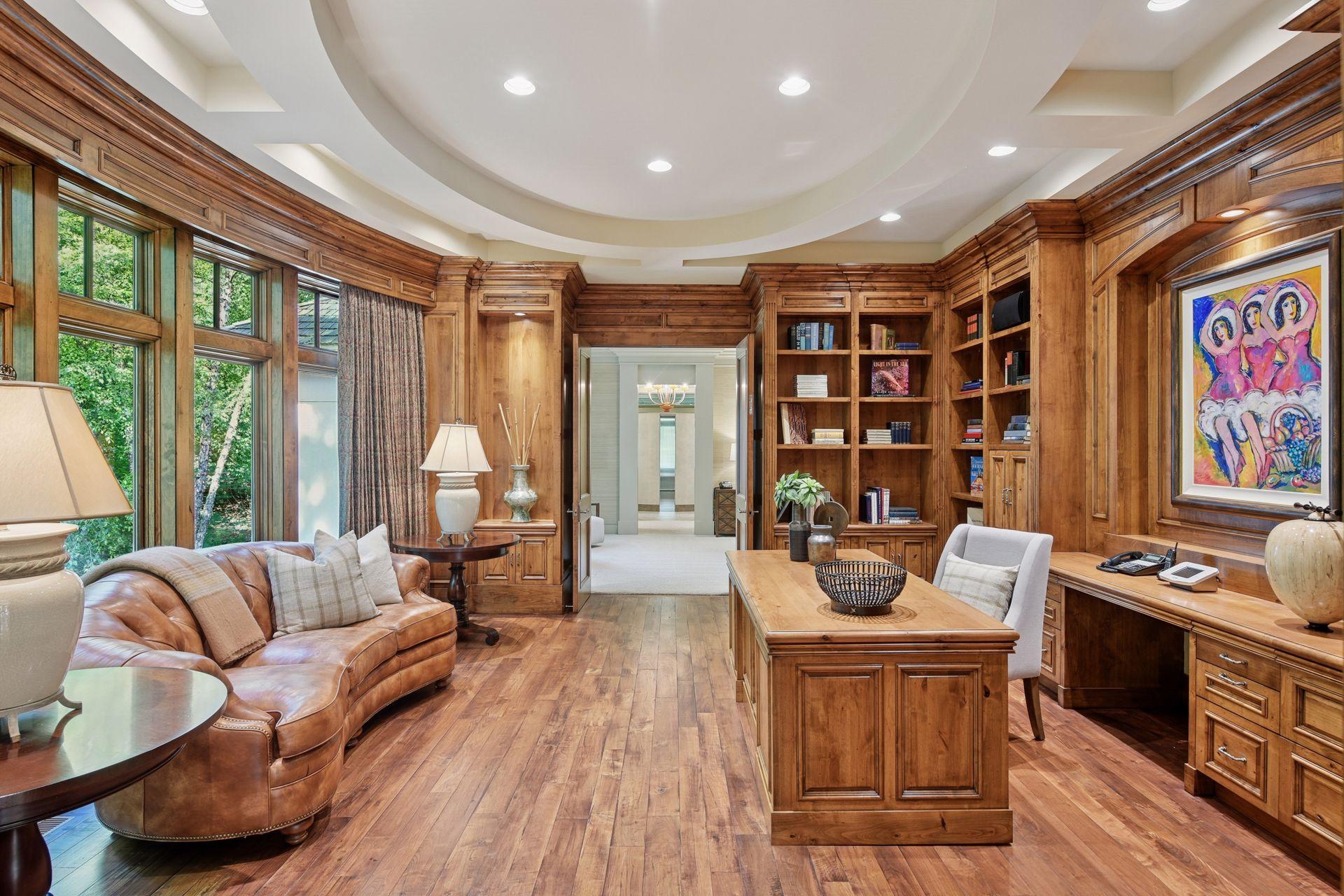 Elegant library with rich wood flooring, built-in shelving, and detailed ceiling accents, offering serene views of the wooded yard.