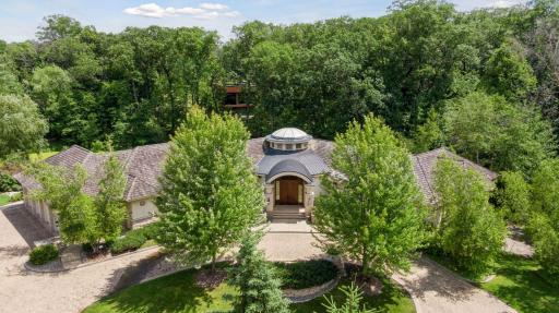 Elegant front approach with an impressive entryway, broad curved paver driveway, and thoughtfully designed gardens.