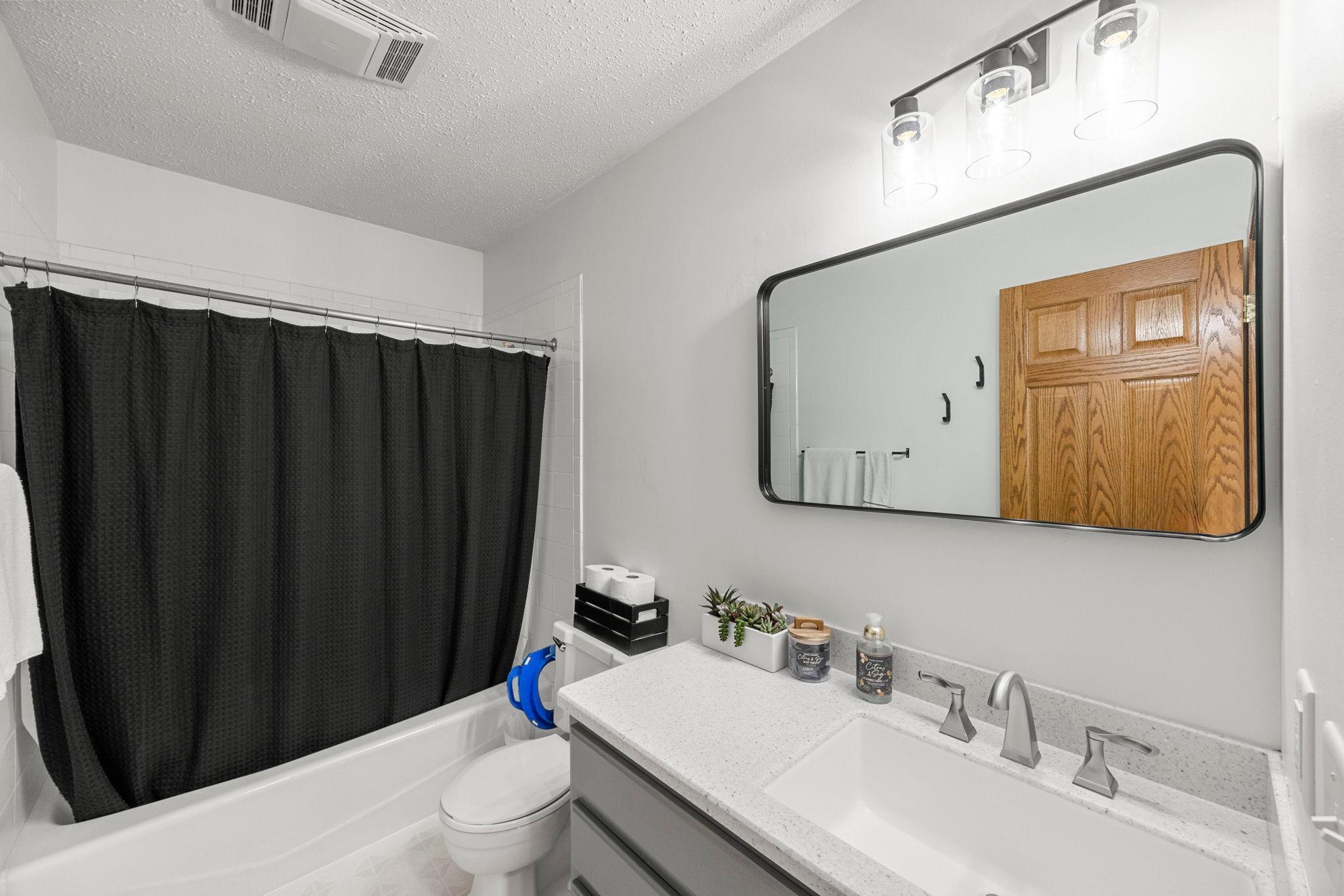 Nearby full bathroom with a tiled tub/shower, vanity, and hallway storage.