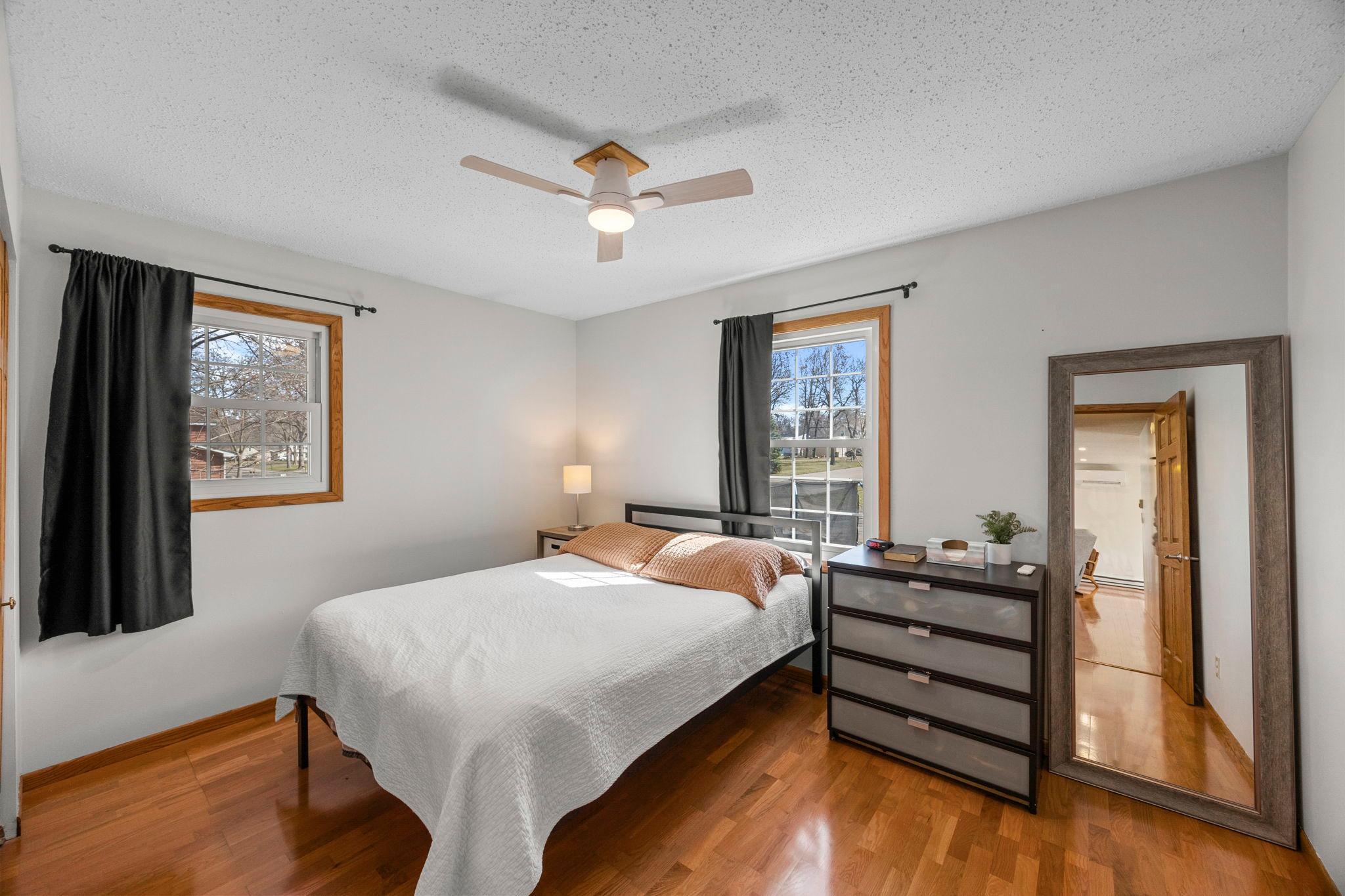 The upper-level bedroom works well as a private primary space, with a ceiling fan, wood flooring and closet space.