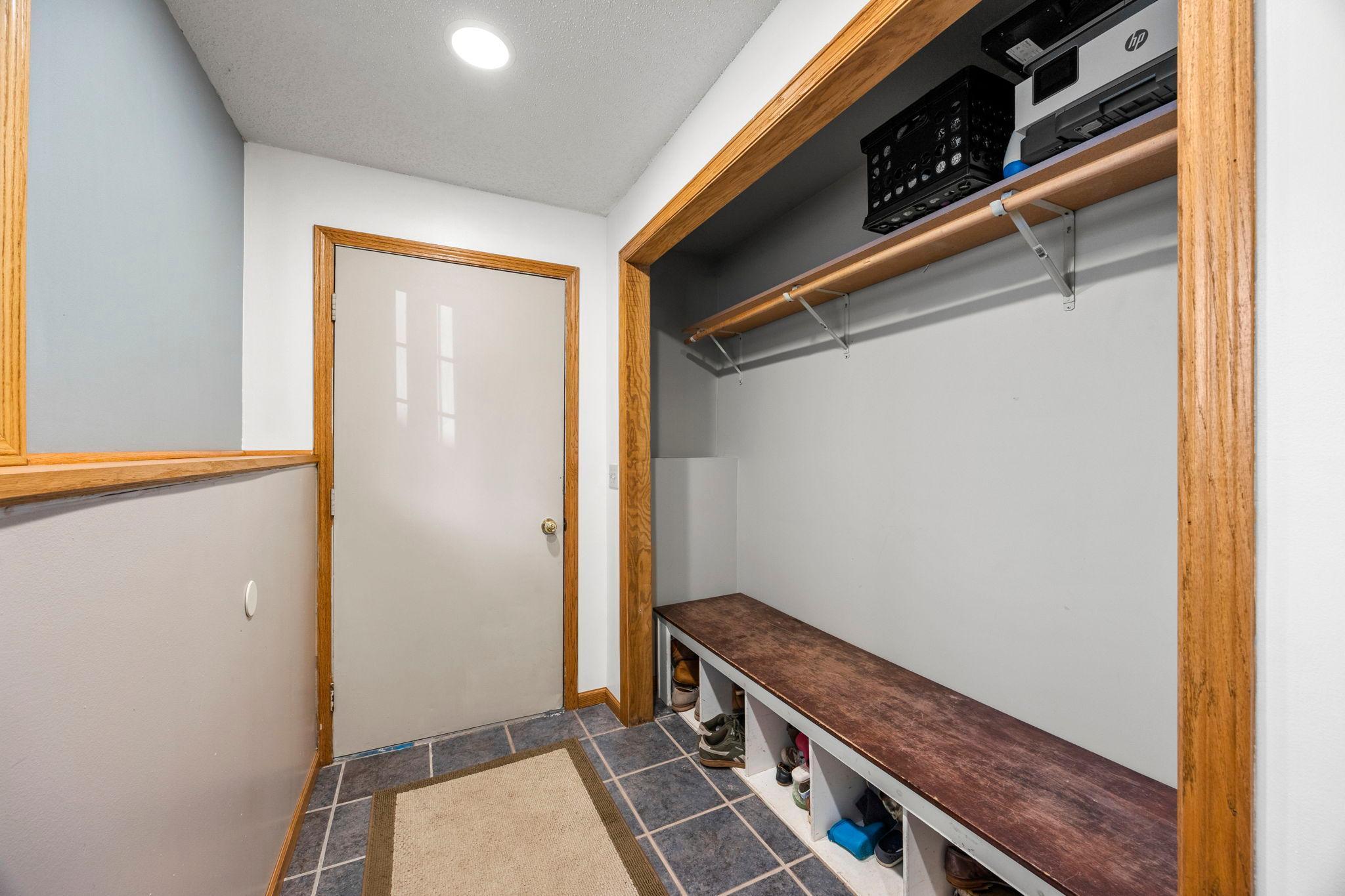 The mudroom offers a practical everyday entry with tile floors, bench seating, a large closet, and access to the attached one-car garage. The finished laundry room includes a Whirlpool washer and dryer, utility sink, and extra cabinetry for storage.