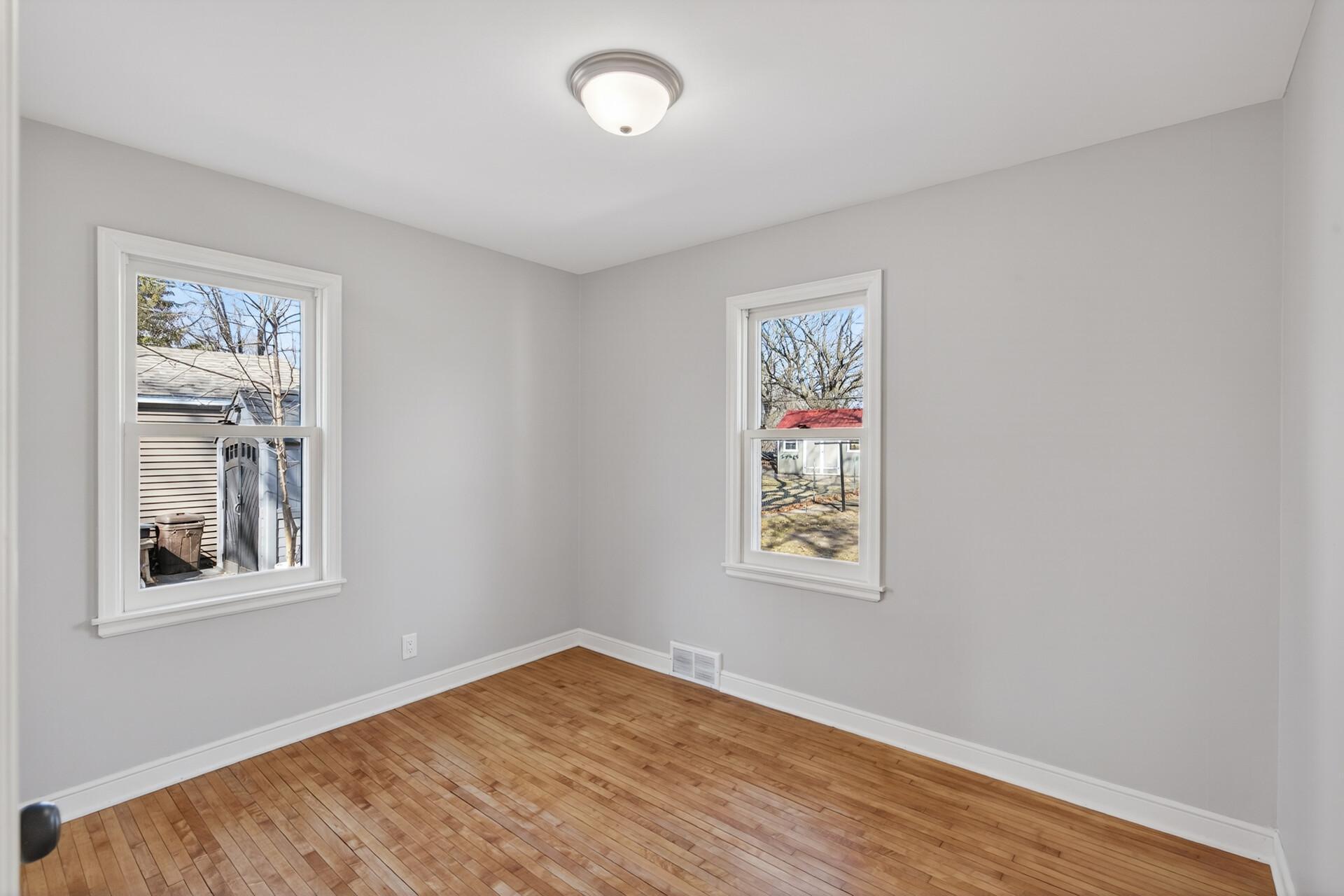 The first main floor bedroom boasts hardwood floors, neutral paint, and dual windows.