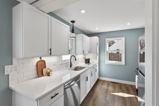 The beautifully updated kitchen showcases crisp white cabinetry, quartz countertops, a stylish tile backsplash, and LVP flooring.