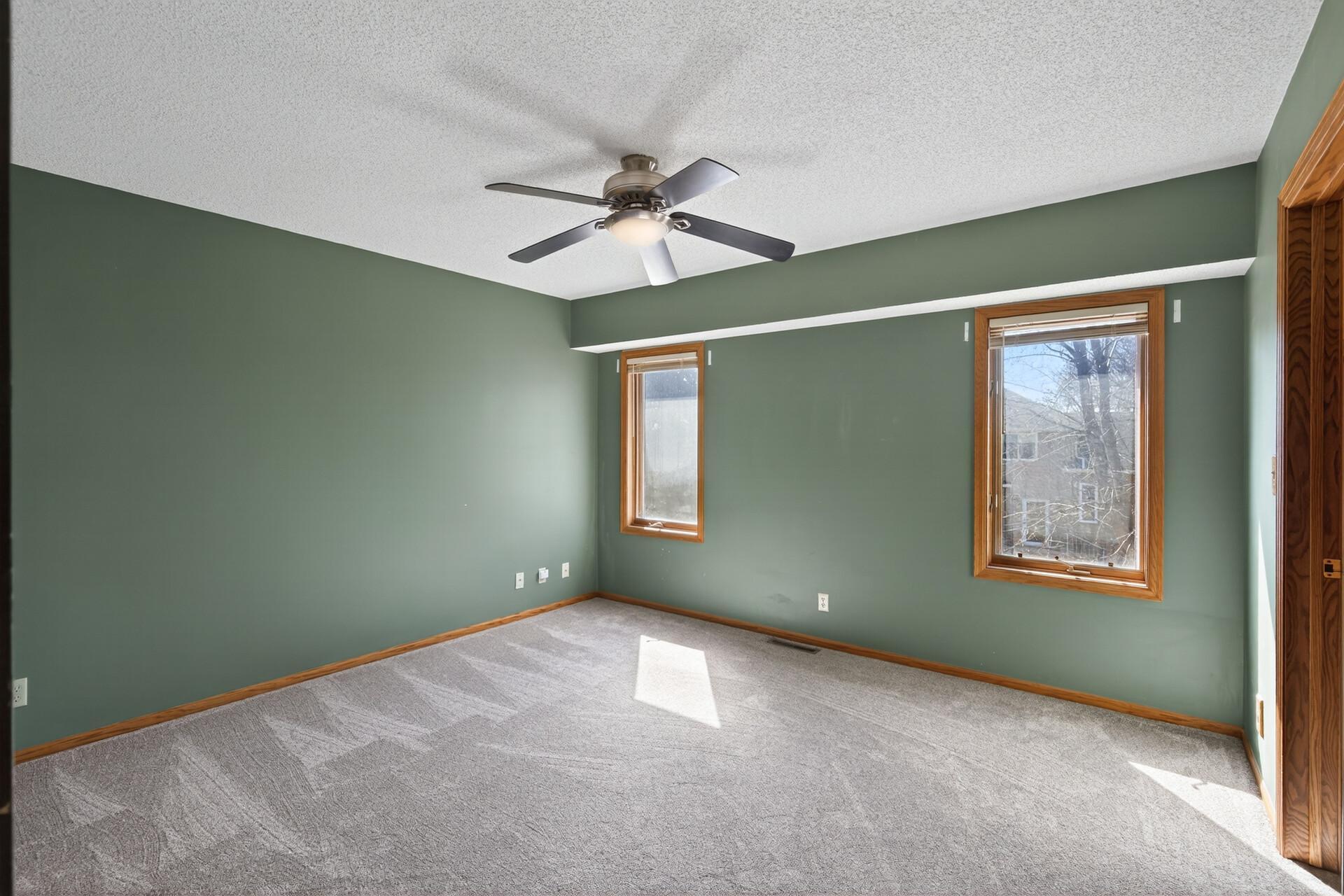 The primary bedroom is generous in size with plush carpeting, dual windows, and a ceiling fan for added comfort.