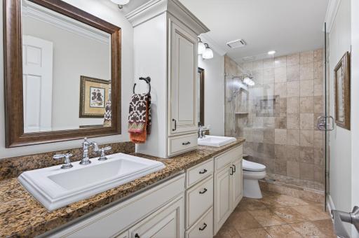 First bath features dual sinks, lots of storage, glass shower surround and tile finishes