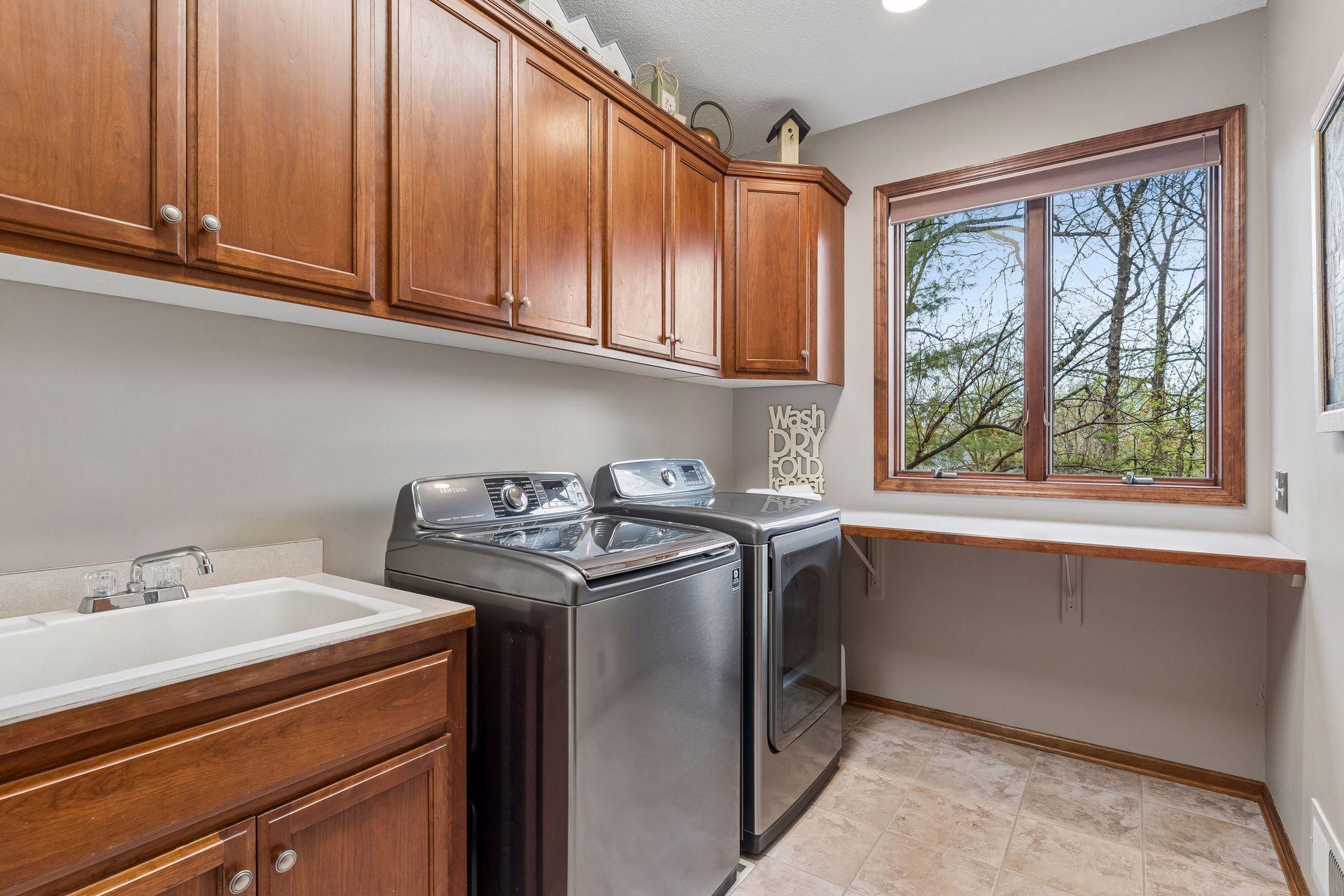 Main level laundry room with abundant cabinetry and counter space, stainless washer/dryer and a convenient laundry sink.