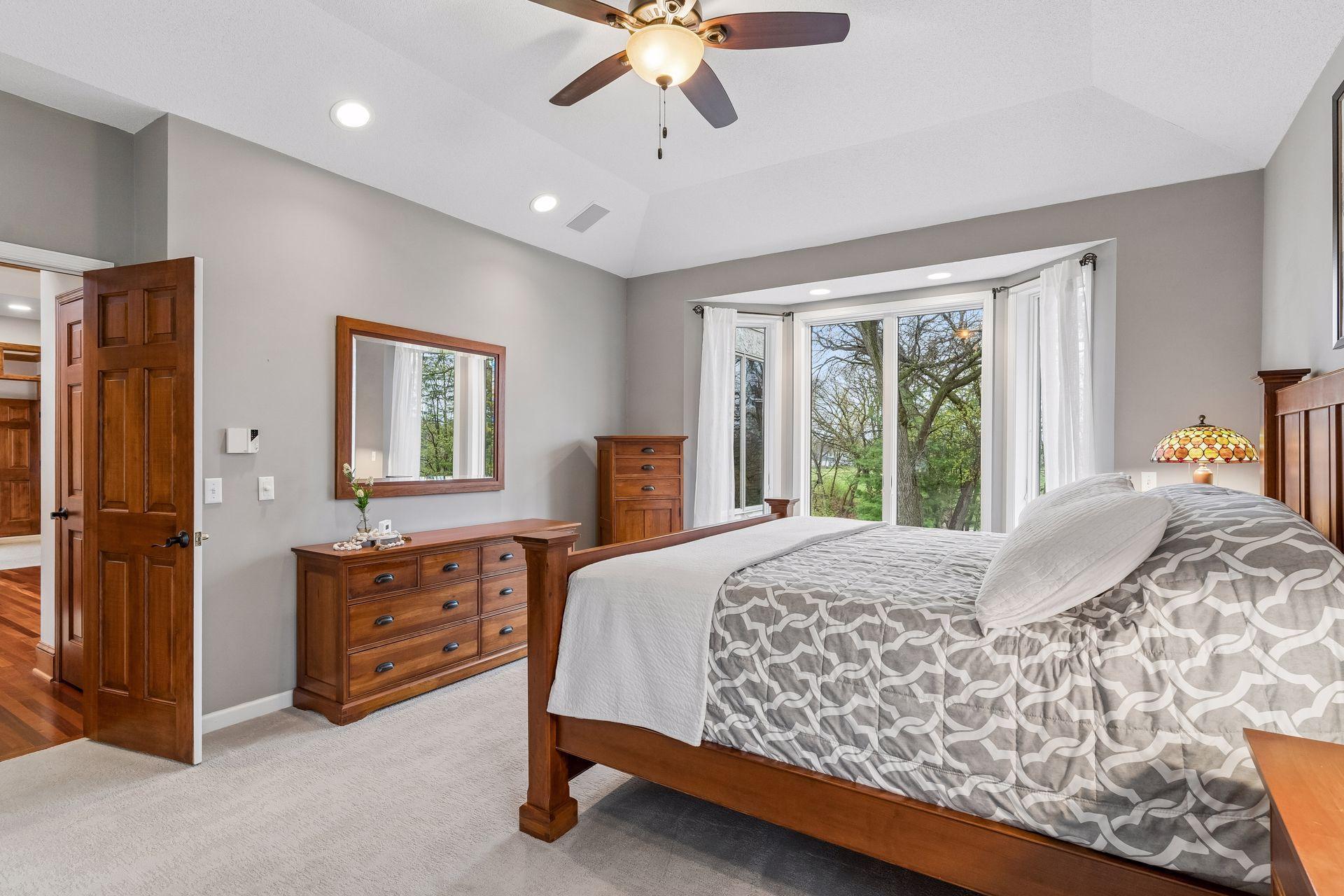 A second view of the primary suite complete with a tray vault ceiling detail and decorative ceiling fan.