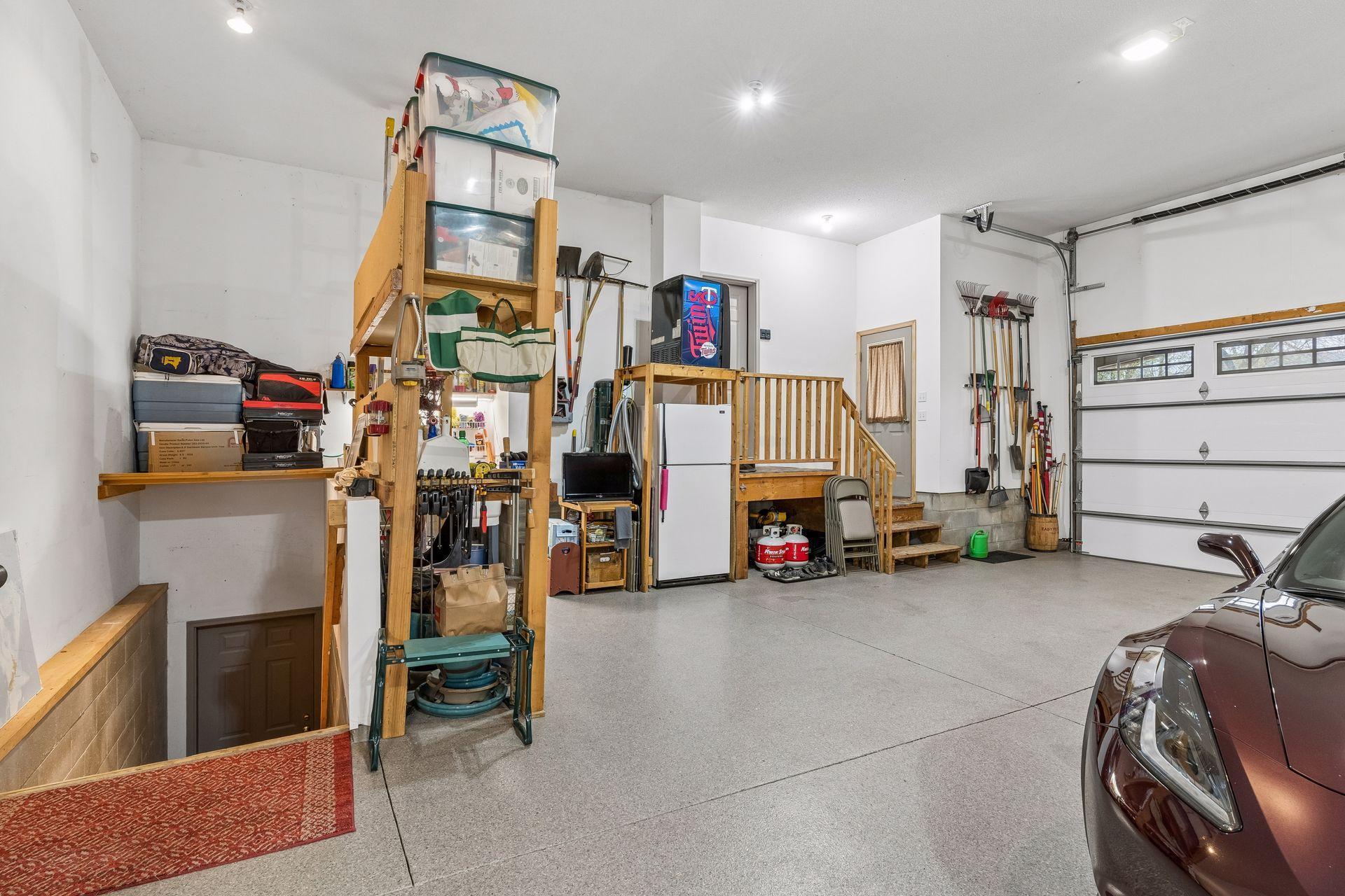 Convenient interior garage staircase that enters into the lower level bonus room/workshop. Plus, abundant built-in storage cabinetry, shelving and refrigerator - all included with the sale of this home.