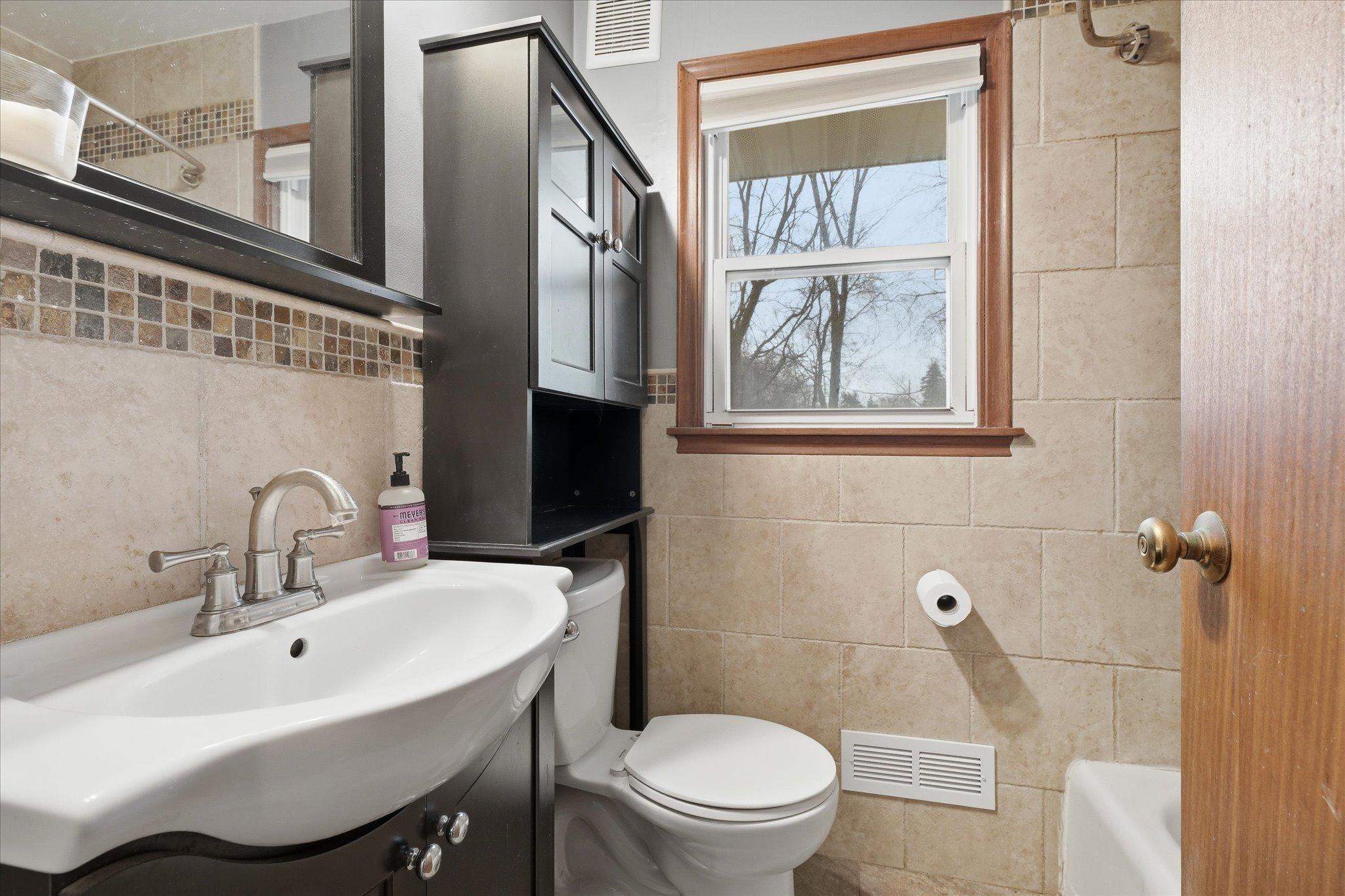 Stylishly updated bathroom featuring tile surround, modern vanity, and a convenient window for natural light.